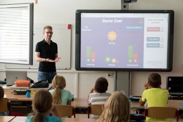 Un enseignant explique devant un tableau interactif affichant un jeu éducatif, idéal pour enseigner les institutions françaises.