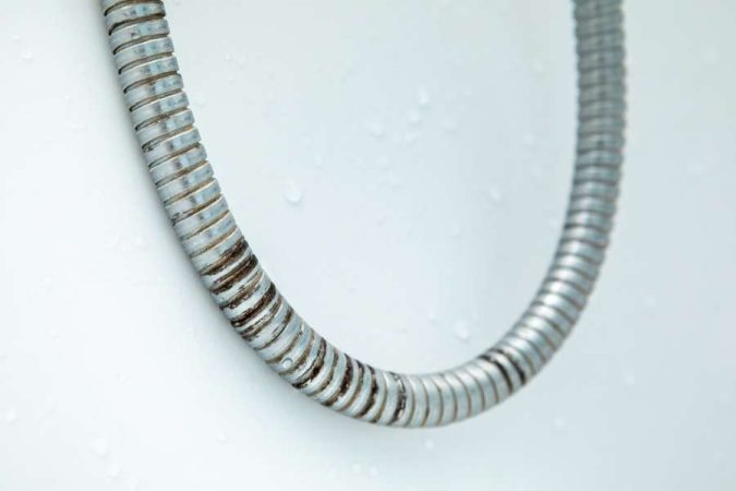 Un flexible de douche métallique comportant des traces de calcaire et de saleté incrustées.